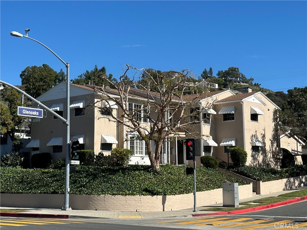Beige two-story apartment with white awnings, greenery, and Glenoaks corner sign