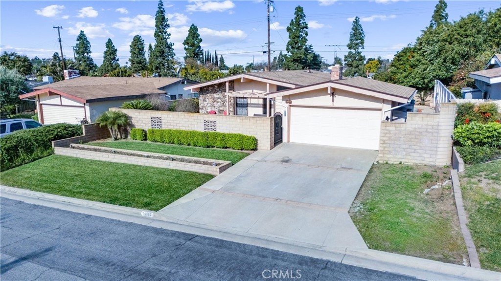 Single-story beige home with lawn, hedges, sloped driveway, and double garage