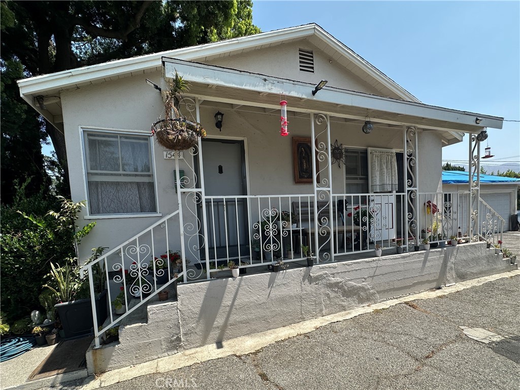 Small white house with porch, hanging plants, and hummingbird feeder on sunny day
