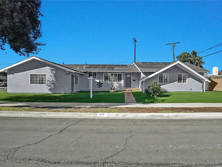 Single-story gray house with solar panels, green lawn, tree, and clear blue sky