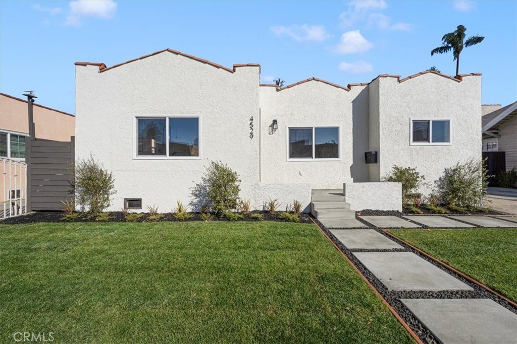 Single-story white stucco house with flat roof, modern path, lawn, and shrubs