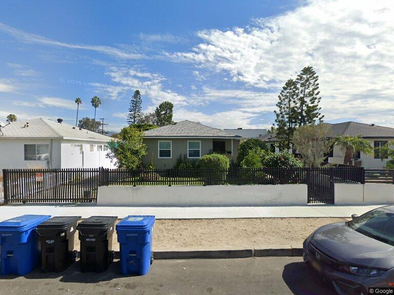 Quiet residential street with single-story homes, fenced yard, trees