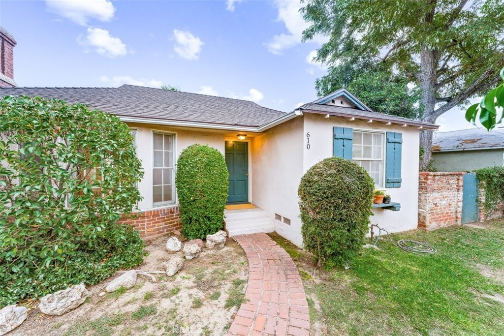 Charming house with brick path, green door, blue shutters, and lush bushes