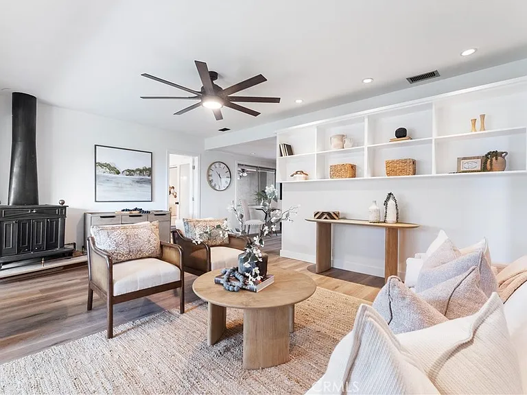 Bright modern living room with white walls, wood floor, neutral seating, plants, and stove