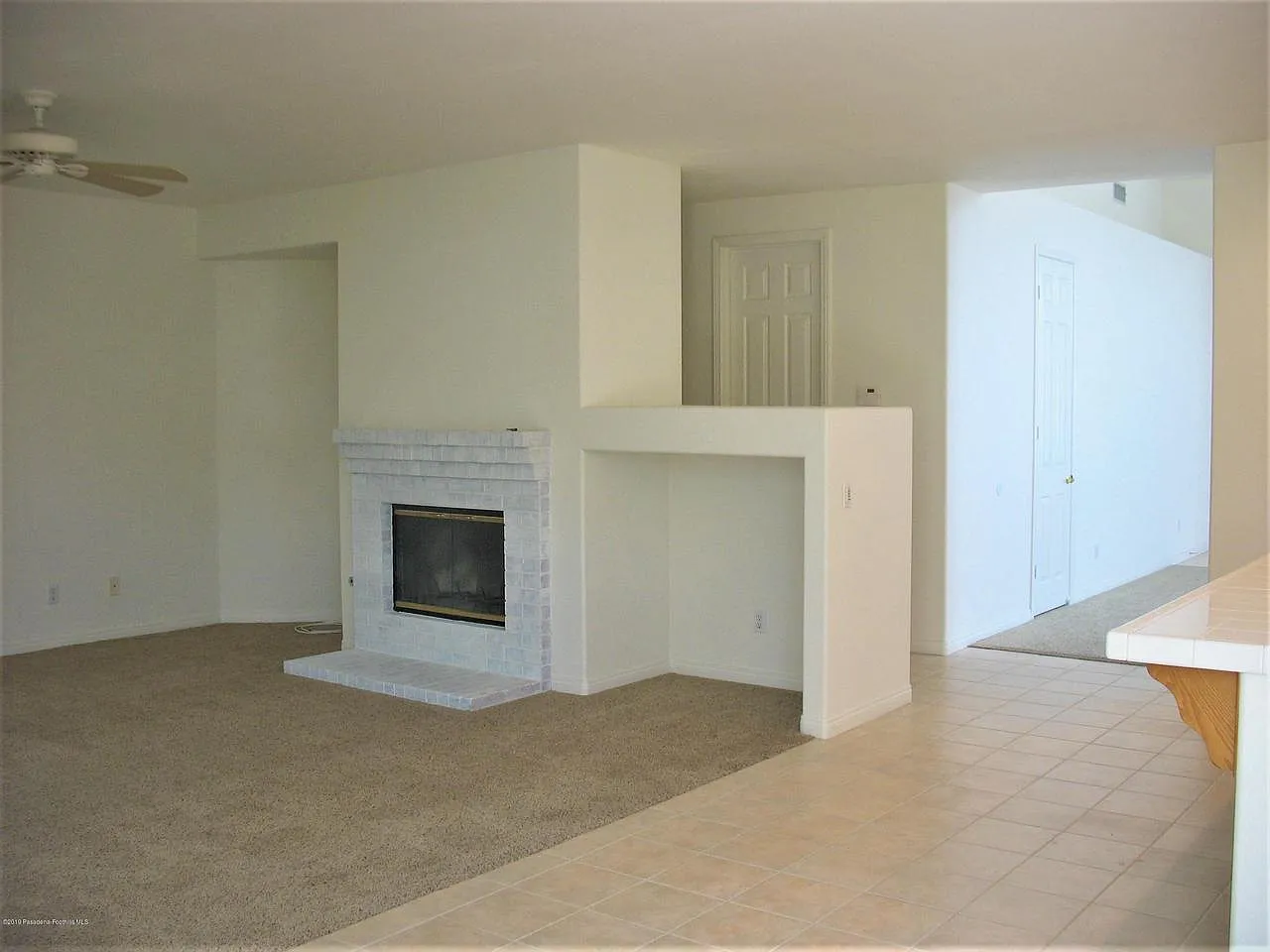Spacious living room with white brick fireplace, carpet, tile floor, and neutral tones