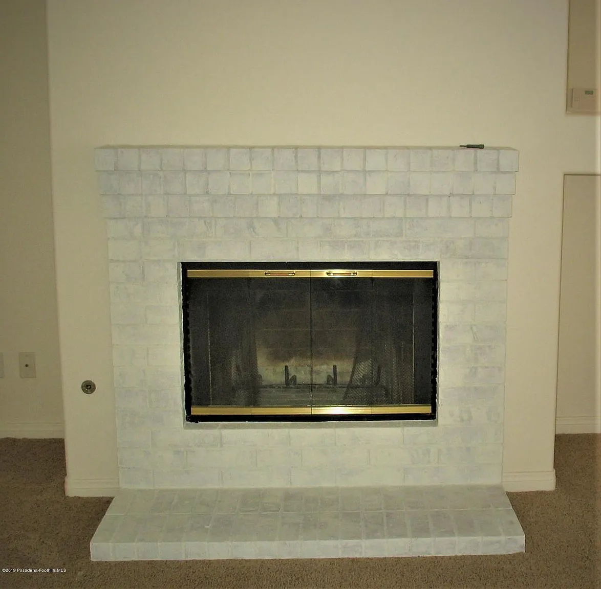 White brick fireplace with gold glass door in beige carpeted room
