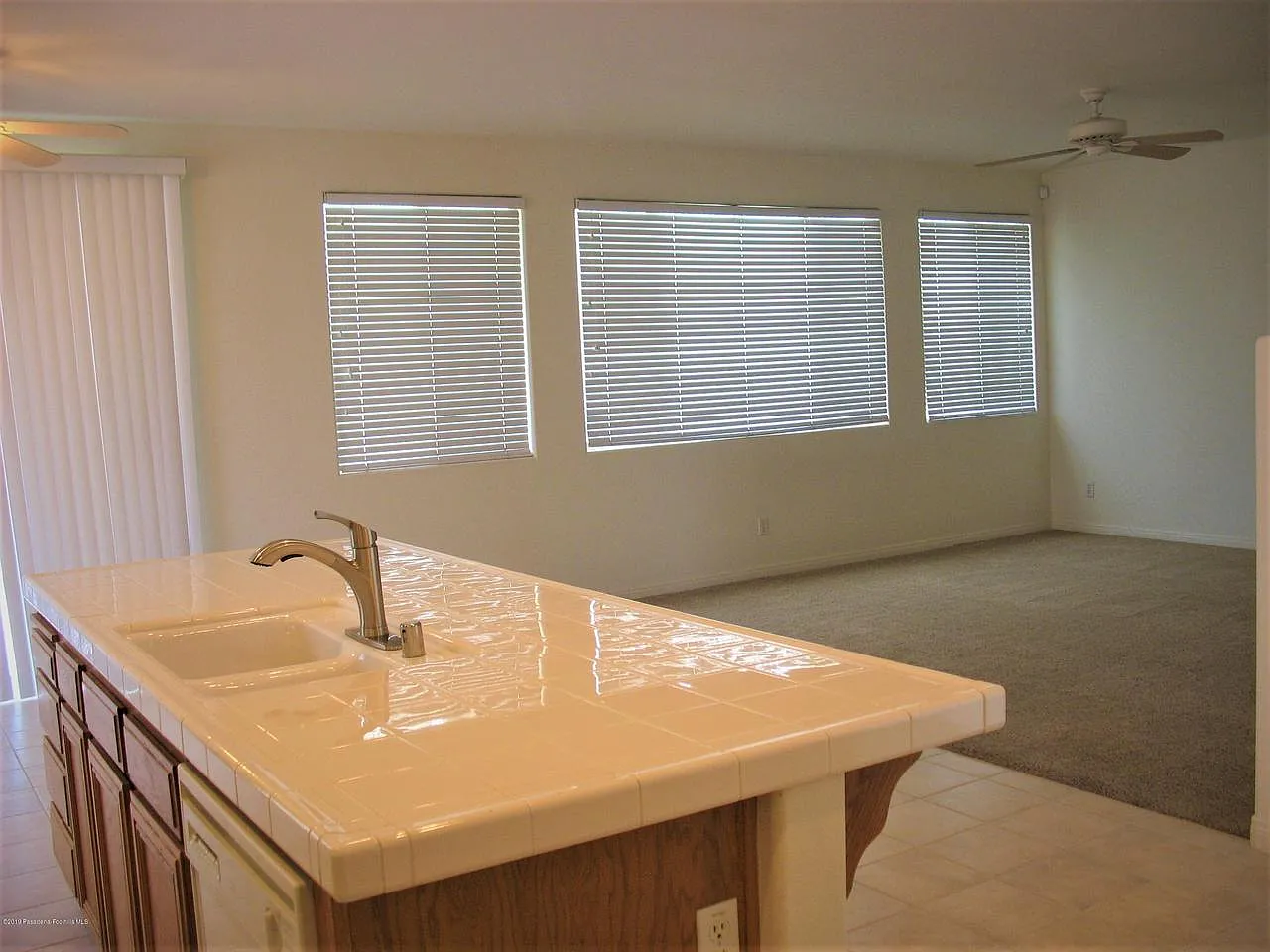 Bright kitchen with tile counter and sink, open to living area with large windows
