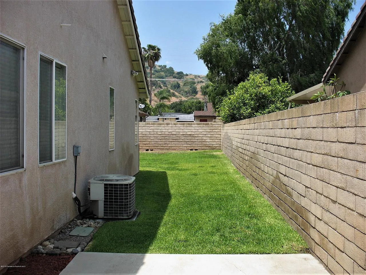 Narrow lawn between stucco house and hedge under clear sky