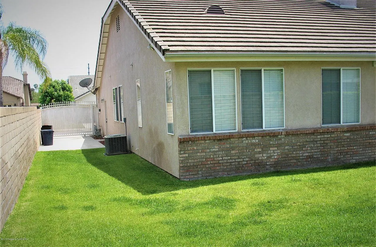 Narrow lawn between stucco house and hedge under clear sky