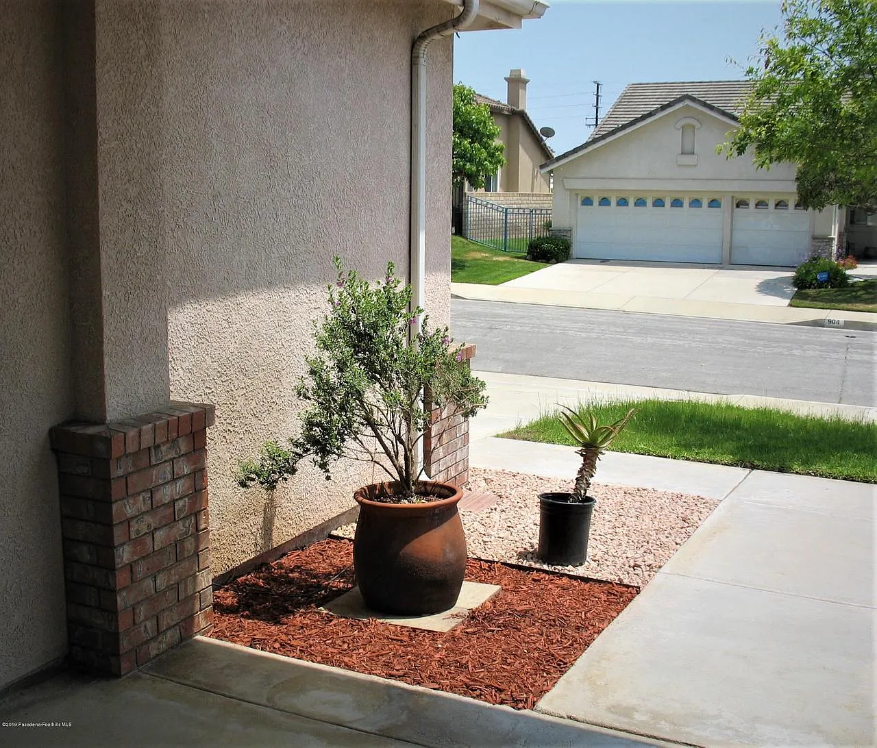 Driveway with potted plant, red mulch, brick wall, and suburban homes in background