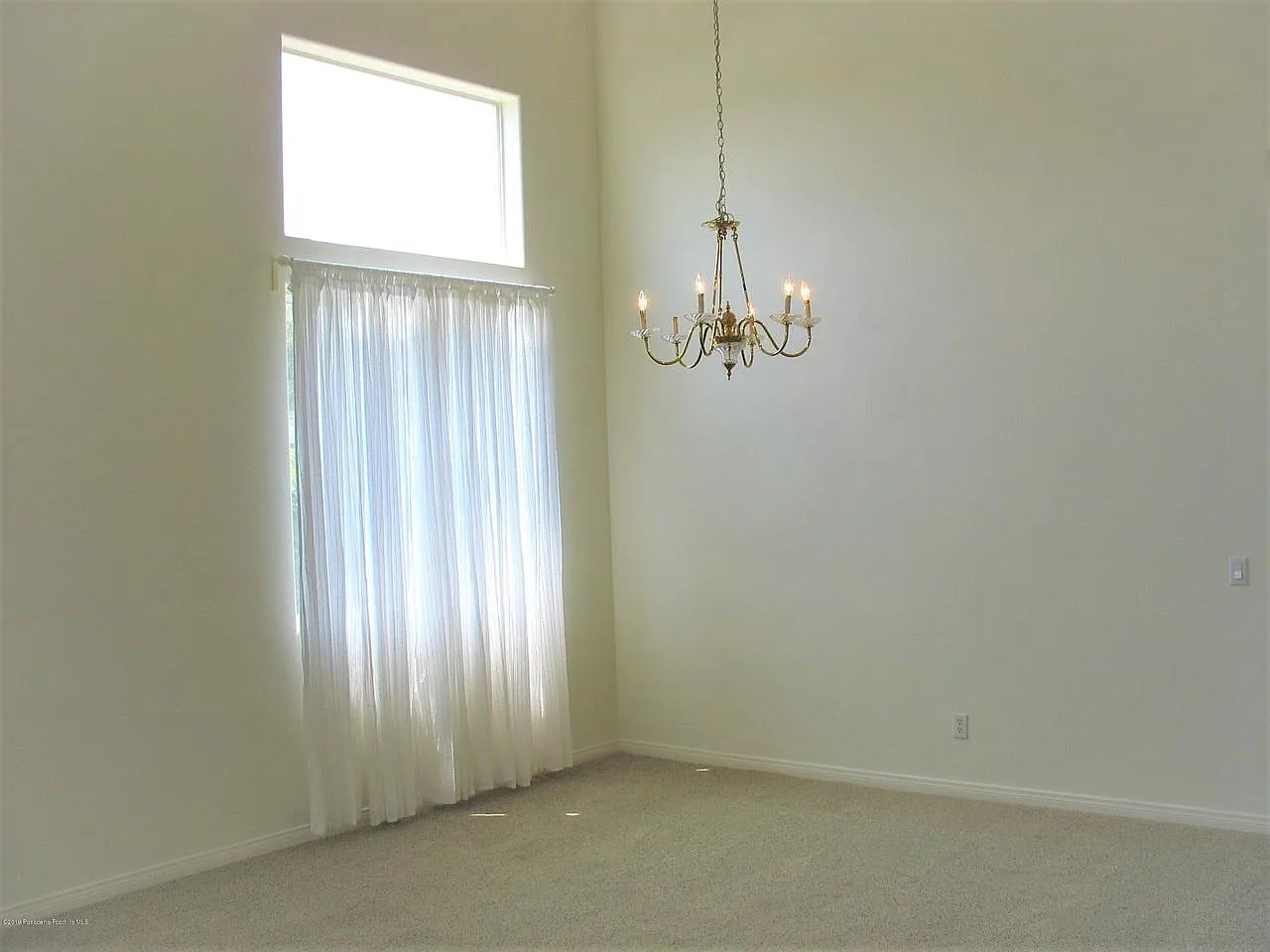 Spacious room with high ceilings, tall window, sheer curtains, and chandelier