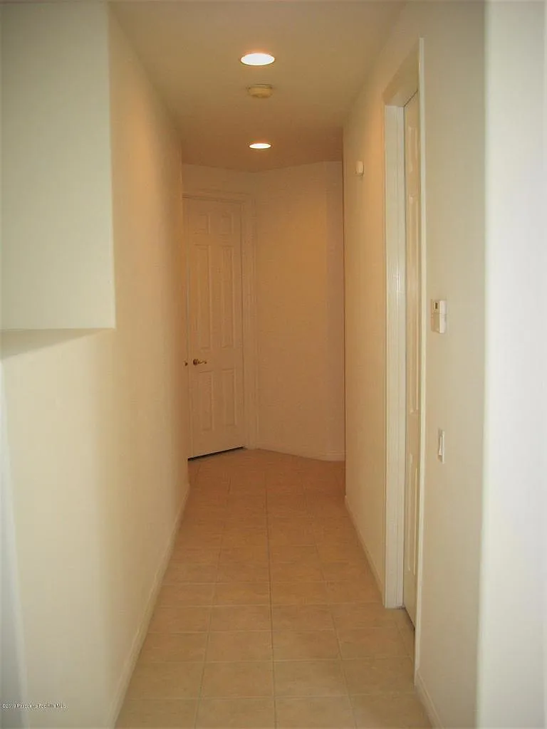 Narrow hallway with beige walls, tiled floor, recessed lights, and white door