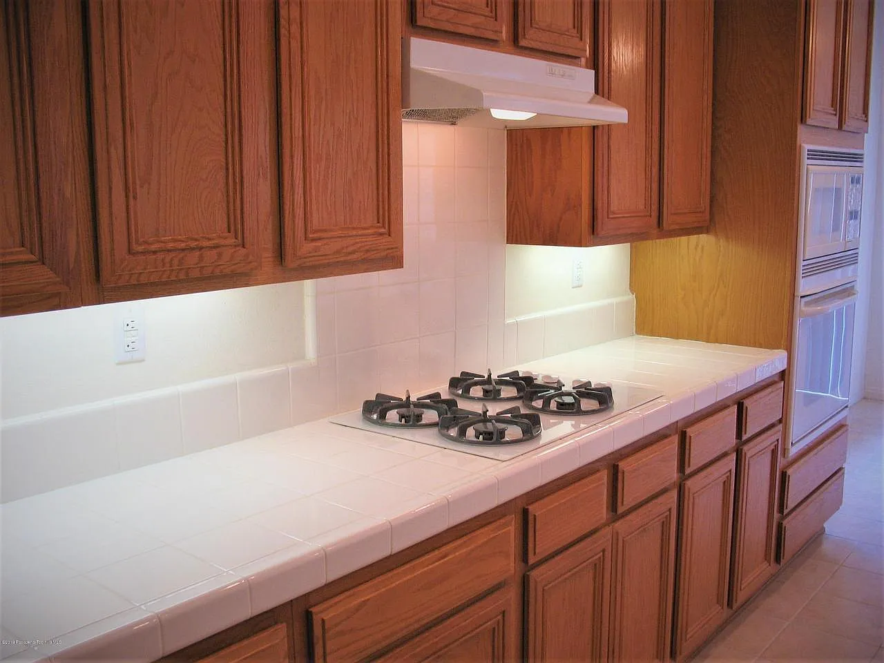 Modern kitchen with wood cabinets, tile counters, gas stove, and built-in oven