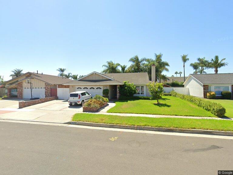 Single-story home with manicured lawn, palm trees, and white SUV on sunny day