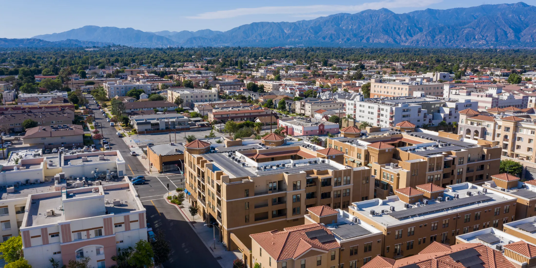 Aerial view of homes, urban buildings, greenery, and mountains