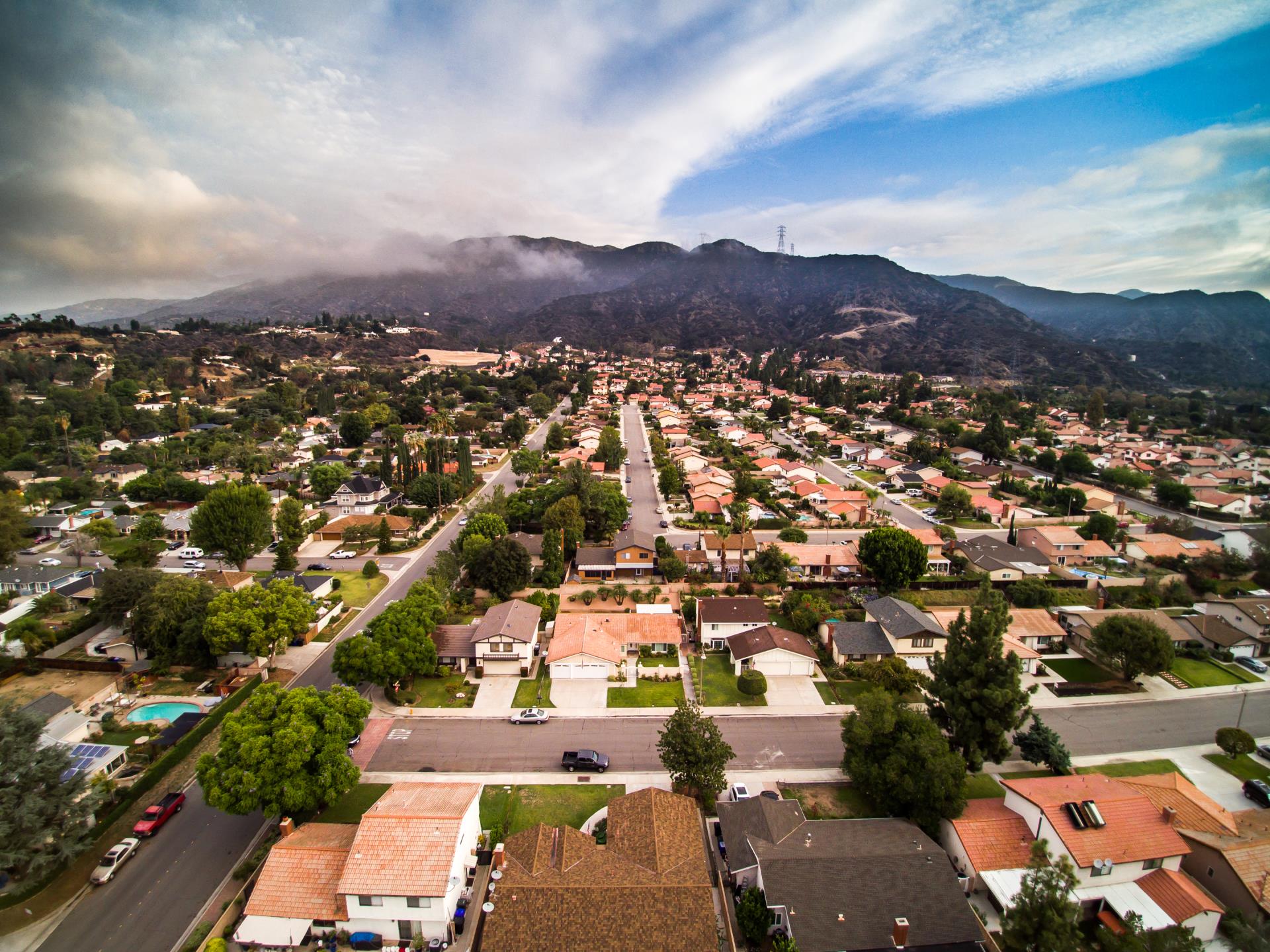 Aerial view of suburban homes, trees, and mountains under cloudy sky