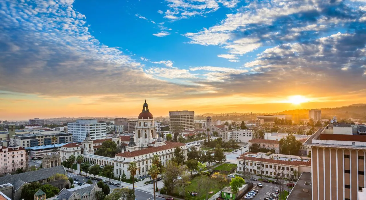 Panoramic city skyline at sunset with dome building, modern towers, greenery, and colorful clouds