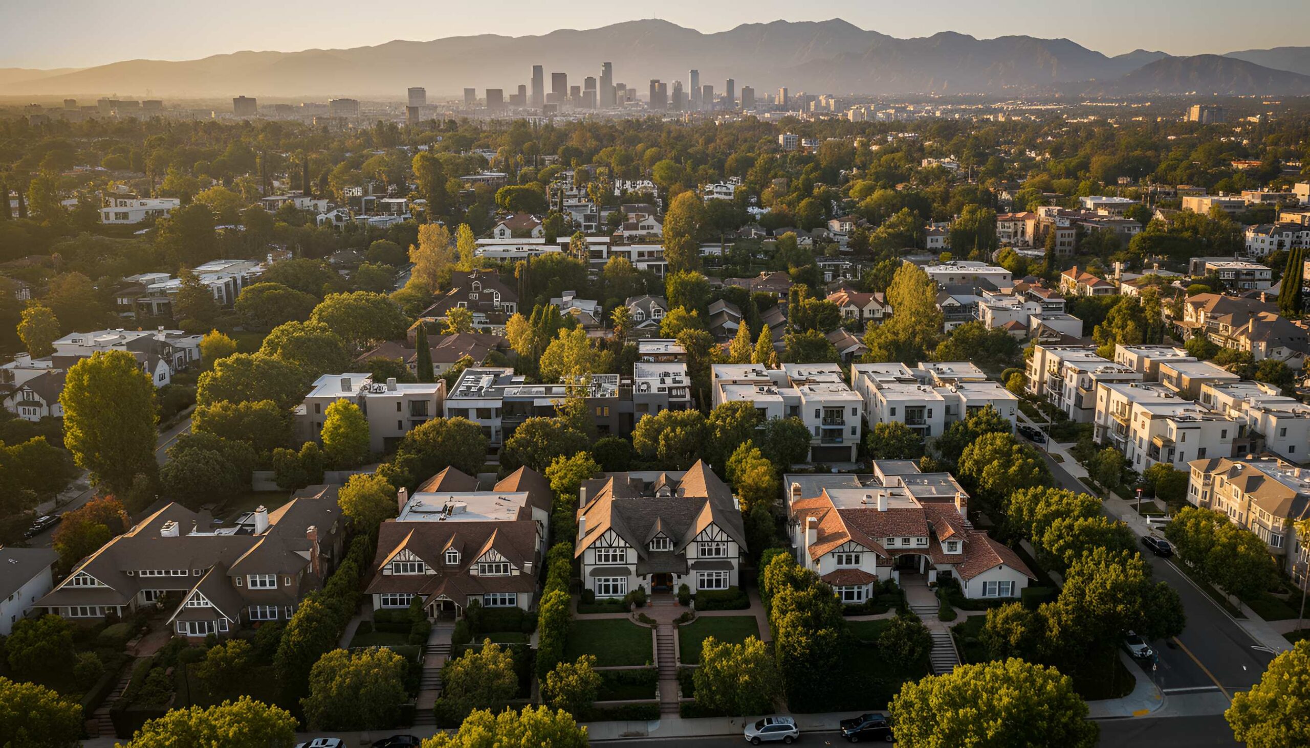 Aerial view of tree-lined suburban homes at sunset with distant skyline and mountains
