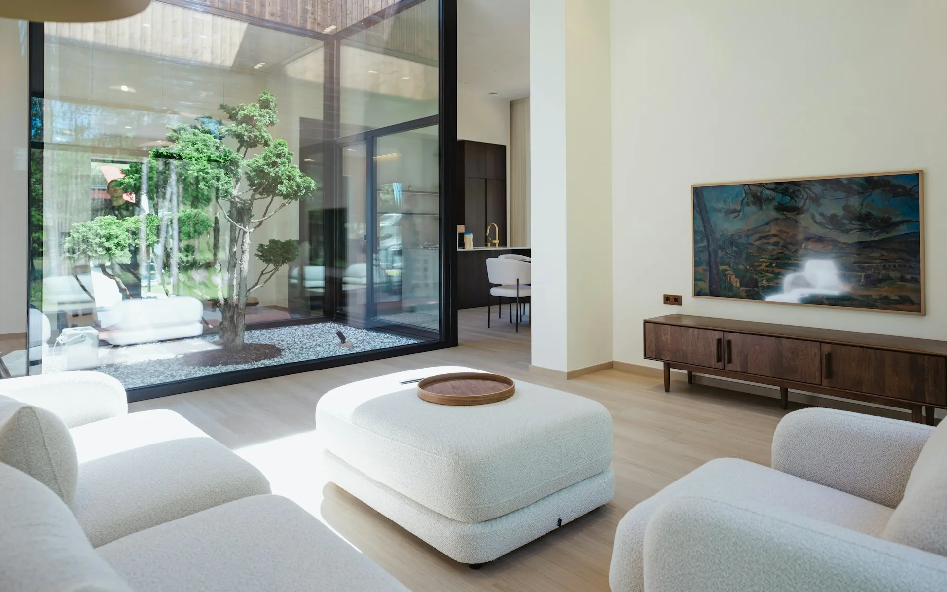 Modern living room with white furniture, courtyard tree view, wood sideboard, and art